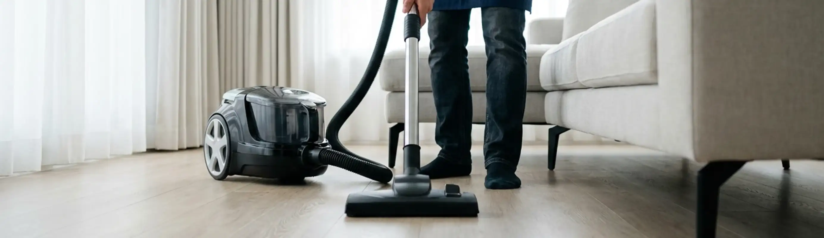 Professional house cleaner vacuuming a living room floor with a canister vacuum cleaner, Oakland, CA.
