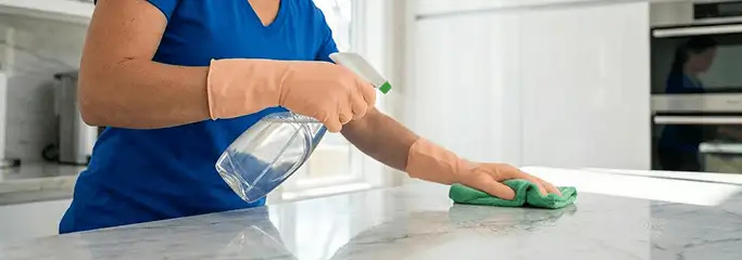 Maid service worker spraying and wiping a kitchen countertop with a microfiber cloth for sanitizing, Oakland, CA.