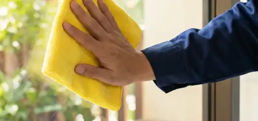 House cleaner wiping a glass window with a yellow microfiber cloth for streak-free cleaning, Oakland, CA.